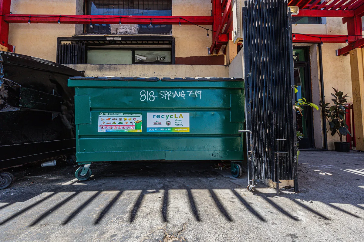 Green food-waste dumpster on the pavement behind a commercial building