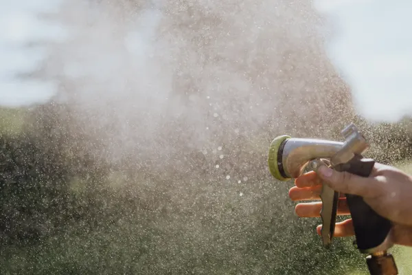 Hand squeezing a garden hose spray nozzle, water misting across a yard