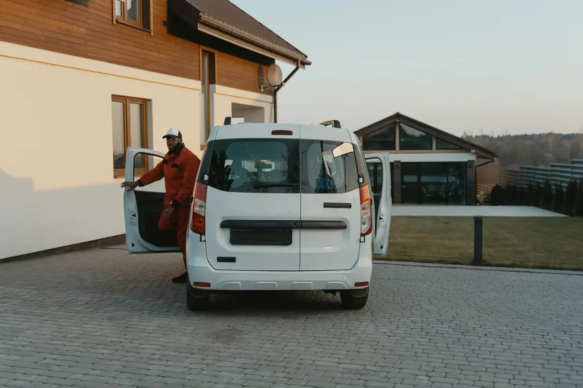 Uniformed service technician stepping out of a white work van in a residential driveway